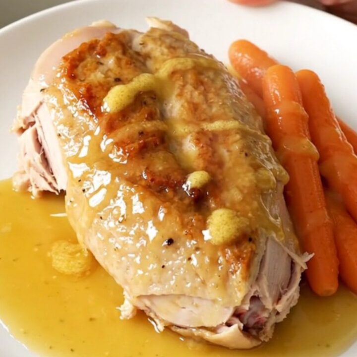 A whole boneless turkey breast and baby carrots in a slow cooker with a honey butter glaze.