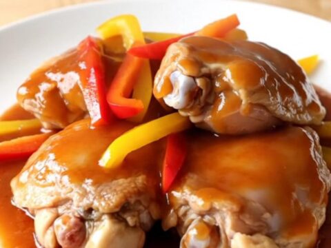 A white slow cooker filled with chicken thighs, colorful peppers, and a glossy sweet chili glaze.