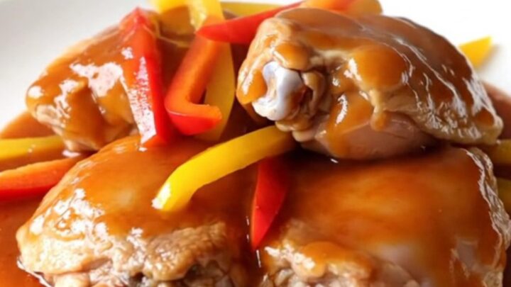 A white slow cooker filled with chicken thighs, colorful peppers, and a glossy sweet chili glaze.