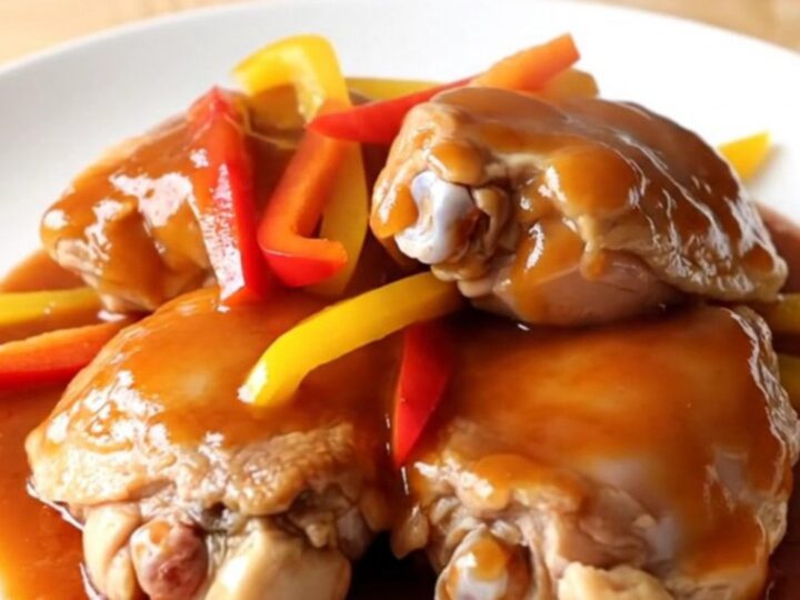 A white slow cooker filled with chicken thighs, colorful peppers, and a glossy sweet chili glaze.