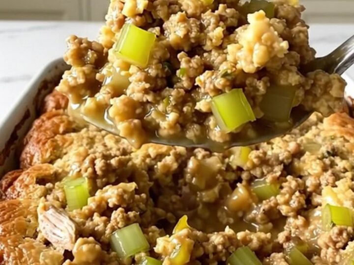 A top-down view of a rectangular ceramic dish filled with ground turkey, gravy, and herb stuffing before baking.