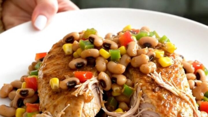 A close-up of slow-cooked chicken breasts topped with a colorful mixture of black-eyed peas, corn, and diced peppers.