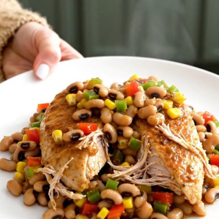 A close-up of slow-cooked chicken breasts topped with a colorful mixture of black-eyed peas, corn, and diced peppers.
