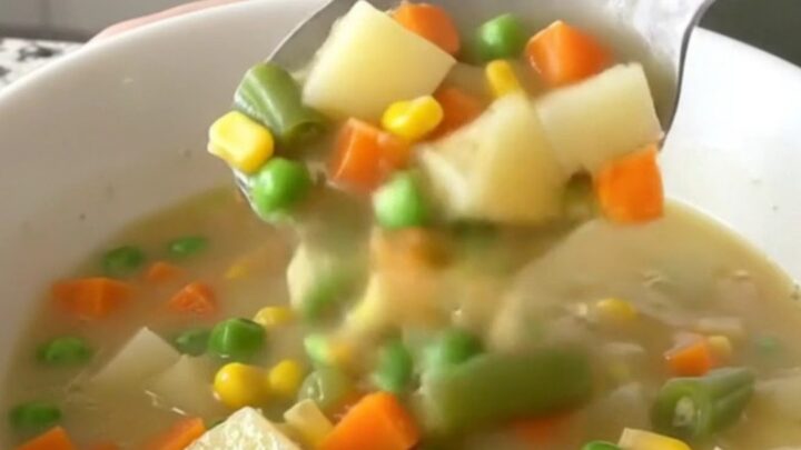 A close-up of creamy vegetable pot pie soup in a white bowl with visible chunks of potatoes and mixed vegetables.