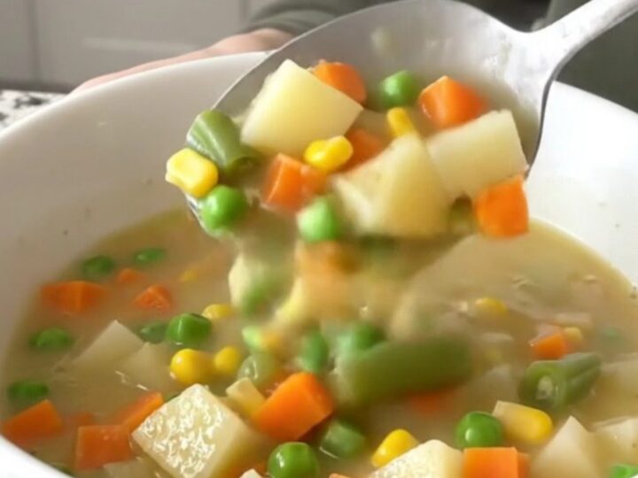 A close-up of creamy vegetable pot pie soup in a white bowl with visible chunks of potatoes and mixed vegetables.