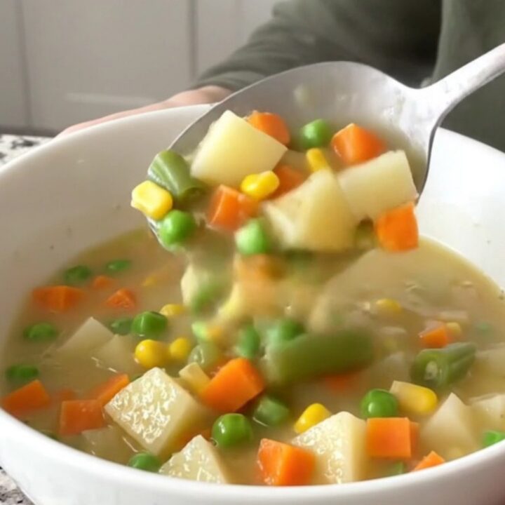 A close-up of creamy vegetable pot pie soup in a white bowl with visible chunks of potatoes and mixed vegetables.