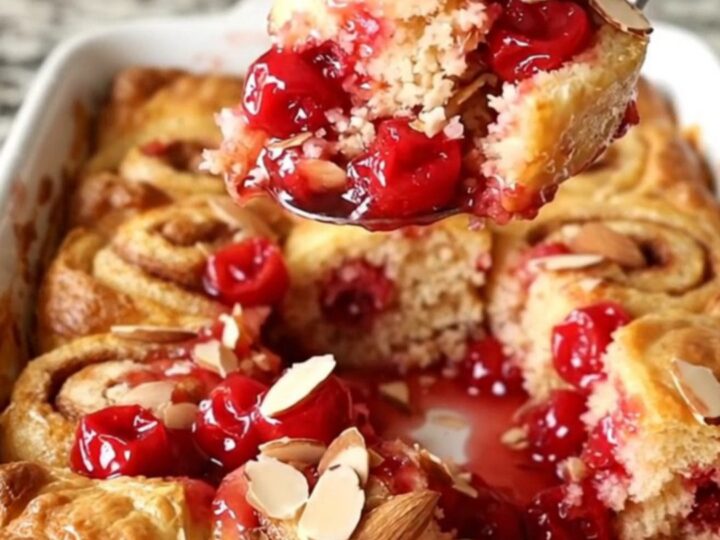 A warm, golden cherry pie cinnamon roll bake in a white ceramic dish with bubbling fruit filling.