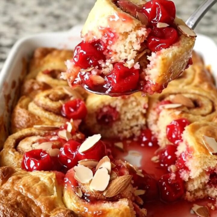 A warm, golden cherry pie cinnamon roll bake in a white ceramic dish with bubbling fruit filling.
