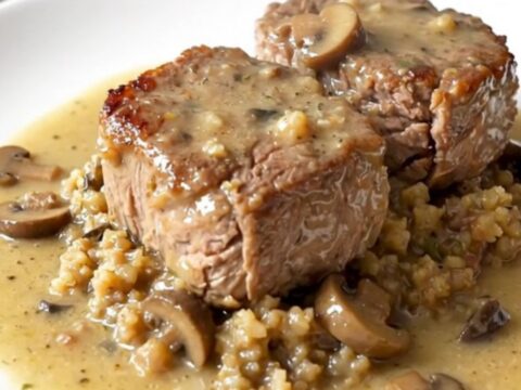 A close-up of tender cube steak covered in herb stuffing and creamy mushroom gravy in a black slow cooker.