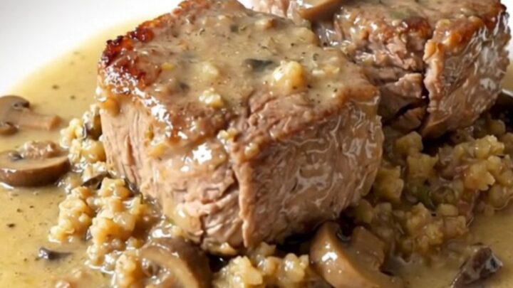 A close-up of tender cube steak covered in herb stuffing and creamy mushroom gravy in a black slow cooker.