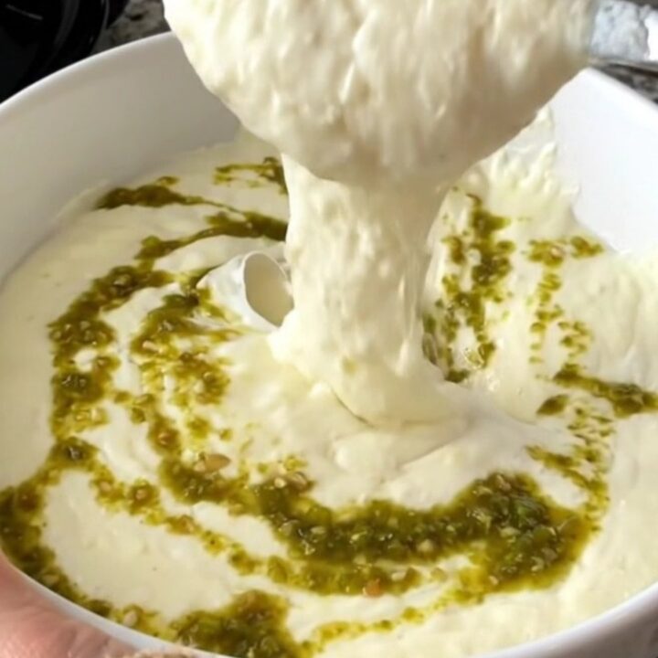 A close-up of thick, melted white queso in a black slow cooker, ready to be served at a party.