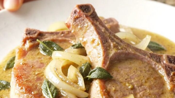 A plate of tender, slow-cooked pork chops covered in a rich, creamy sage gravy with sautéed onions.