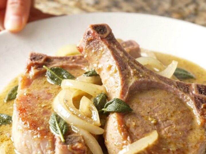 A plate of tender, slow-cooked pork chops covered in a rich, creamy sage gravy with sautéed onions.