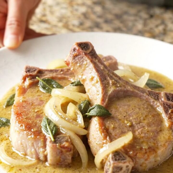 A plate of tender, slow-cooked pork chops covered in a rich, creamy sage gravy with sautéed onions.
