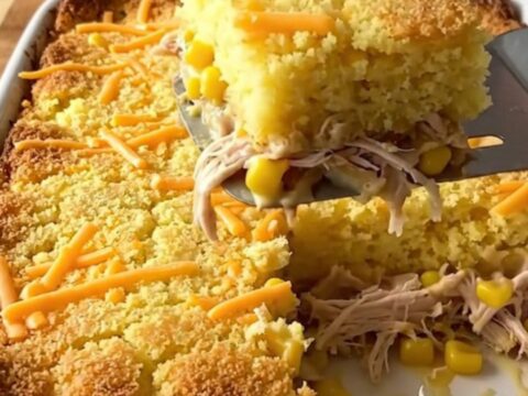 A golden, bubbling square of chicken and cornbread casserole being lifted from a baking dish.