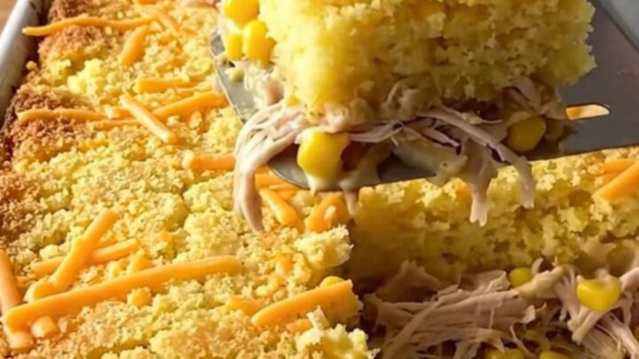 A golden, bubbling square of chicken and cornbread casserole being lifted from a baking dish.