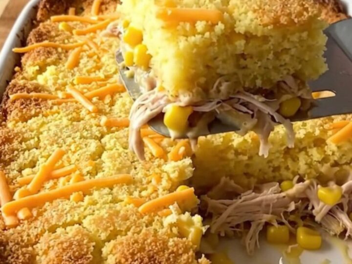 A golden, bubbling square of chicken and cornbread casserole being lifted from a baking dish.