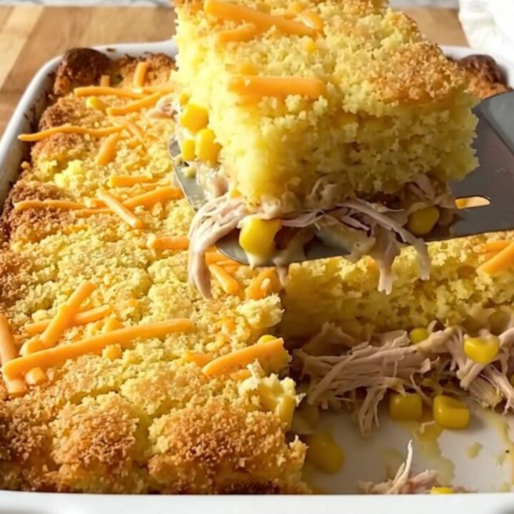 A golden, bubbling square of chicken and cornbread casserole being lifted from a baking dish.