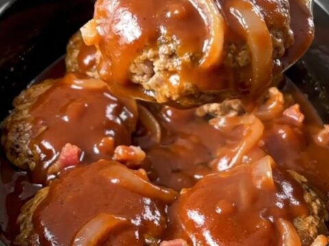 A close-up of slow-cooked turkey burger steaks smothered in a thick, glossy barbecue sauce with bacon and onions.
