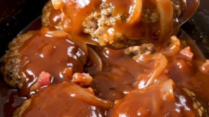 A close-up of slow-cooked turkey burger steaks smothered in a thick, glossy barbecue sauce with bacon and onions.