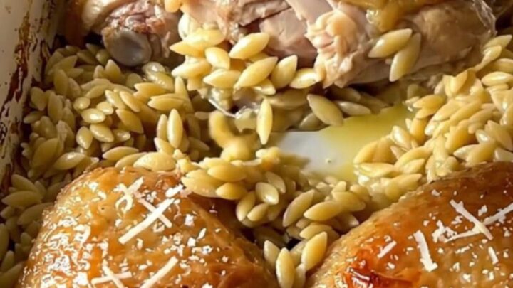 A large rectangular ceramic baking dish filled with golden baked chicken thighs and creamy orzo on a quartz counter.