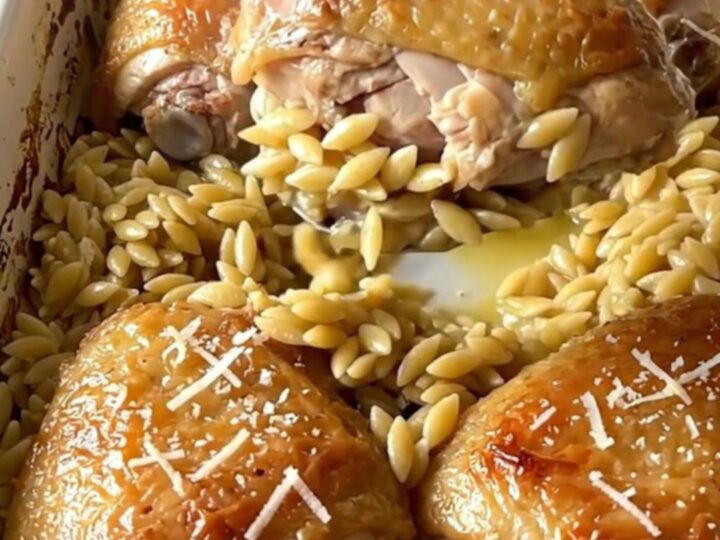 A large rectangular ceramic baking dish filled with golden baked chicken thighs and creamy orzo on a quartz counter.