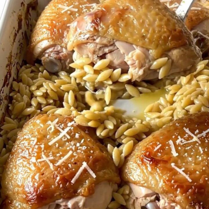 A large rectangular ceramic baking dish filled with golden baked chicken thighs and creamy orzo on a quartz counter.