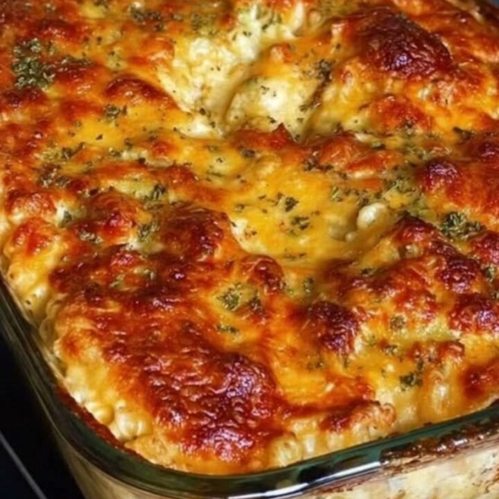 A close-up of a serving spoon lifting creamy, golden-baked macaroni and cheese from a glass dish.