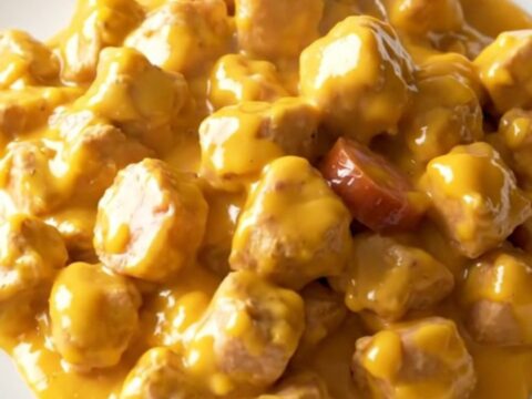A close-up of a plate containing creamy chicken, smoked sausage slices, and tender potatoes in a rich cheddar sauce.
