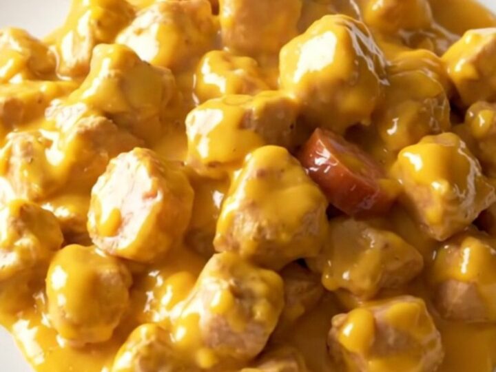 A close-up of a plate containing creamy chicken, smoked sausage slices, and tender potatoes in a rich cheddar sauce.