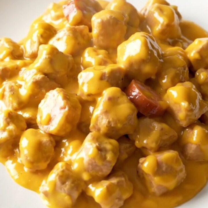 A close-up of a plate containing creamy chicken, smoked sausage slices, and tender potatoes in a rich cheddar sauce.