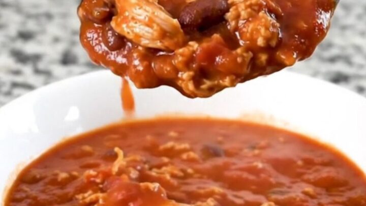 A hearty bowl of smoky turkey and bacon chili in a white bowl with a spoon, steam rising.