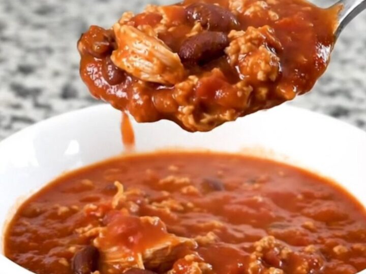A hearty bowl of smoky turkey and bacon chili in a white bowl with a spoon, steam rising.
