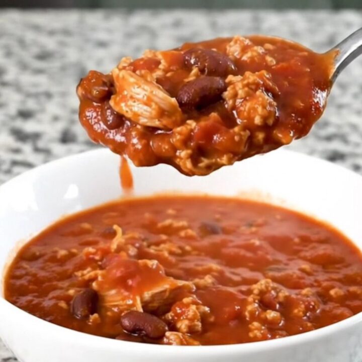 A hearty bowl of smoky turkey and bacon chili in a white bowl with a spoon, steam rising.
