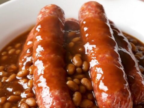 A close-up of raw bratwurst links arranged in a white slow cooker insert before cooking.