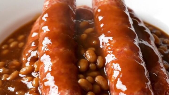 A close-up of raw bratwurst links arranged in a white slow cooker insert before cooking.