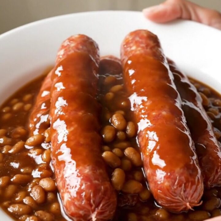 A close-up of raw bratwurst links arranged in a white slow cooker insert before cooking.