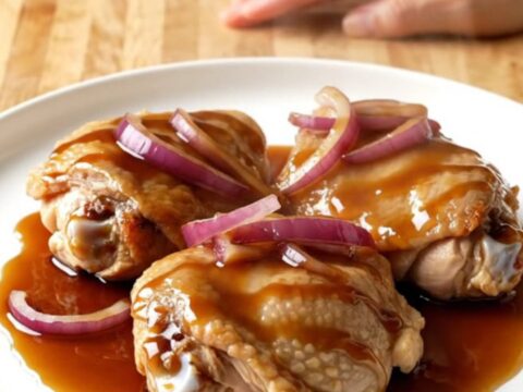 A close-up of tender, braised honey balsamic chicken thighs in a white slow cooker insert.