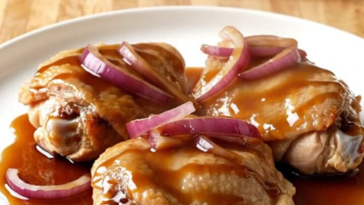 A close-up of tender, braised honey balsamic chicken thighs in a white slow cooker insert.