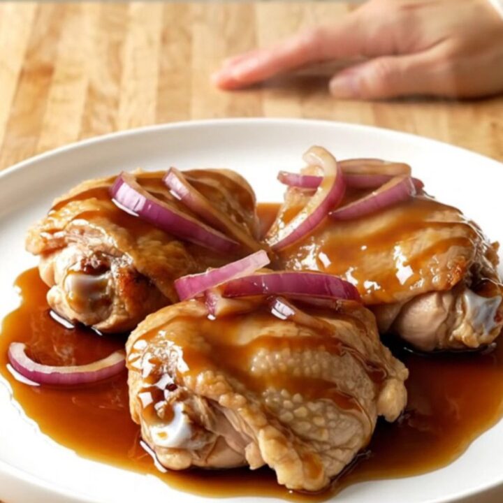 A close-up of tender, braised honey balsamic chicken thighs in a white slow cooker insert.