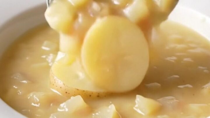 A bowl of creamy potato au gratin soup with visible potato slices and melted cheddar cheese.