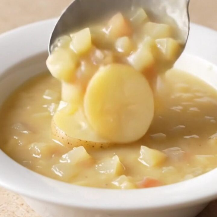 A bowl of creamy potato au gratin soup with visible potato slices and melted cheddar cheese.