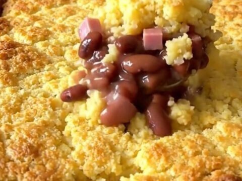 A golden, baked ham and pinto bean cornbread casserole in a white ceramic dish on a kitchen counter.