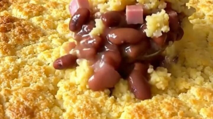 A golden, baked ham and pinto bean cornbread casserole in a white ceramic dish on a kitchen counter.