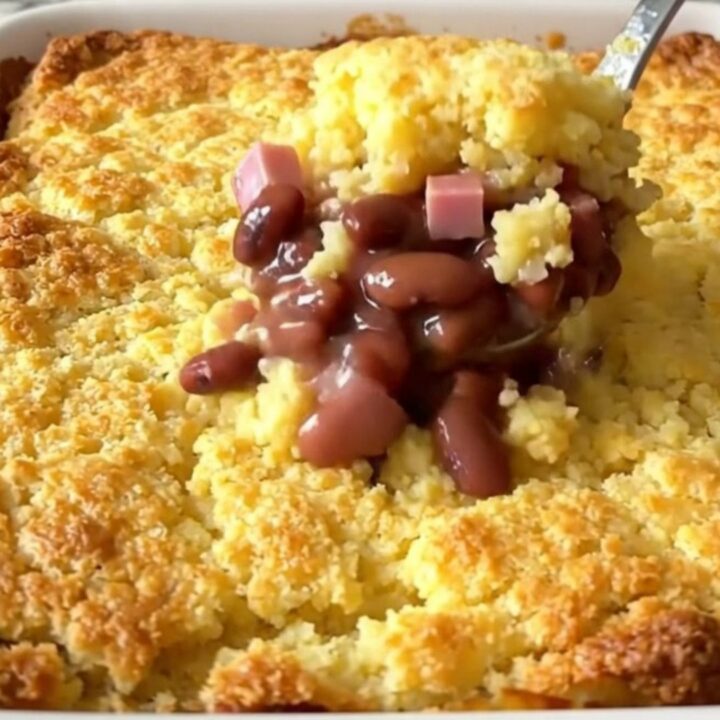 A golden, baked ham and pinto bean cornbread casserole in a white ceramic dish on a kitchen counter.