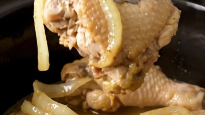 A top-down view of six raw boneless skinless chicken thighs arranged neatly in a black slow cooker insert.