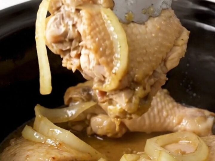 A top-down view of six raw boneless skinless chicken thighs arranged neatly in a black slow cooker insert.