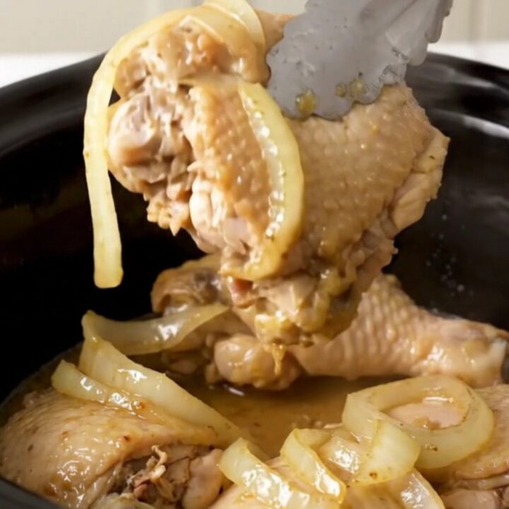 A top-down view of six raw boneless skinless chicken thighs arranged neatly in a black slow cooker insert.