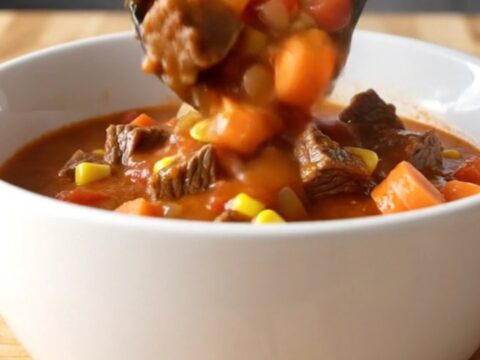 A white shallow bowl filled with beef Mulligan stew featuring tender beef cubes, potatoes, carrots
