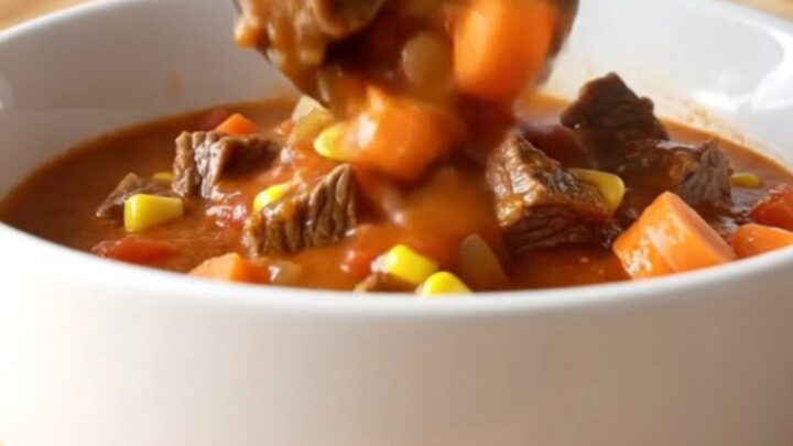 A white shallow bowl filled with beef Mulligan stew featuring tender beef cubes, potatoes, carrots